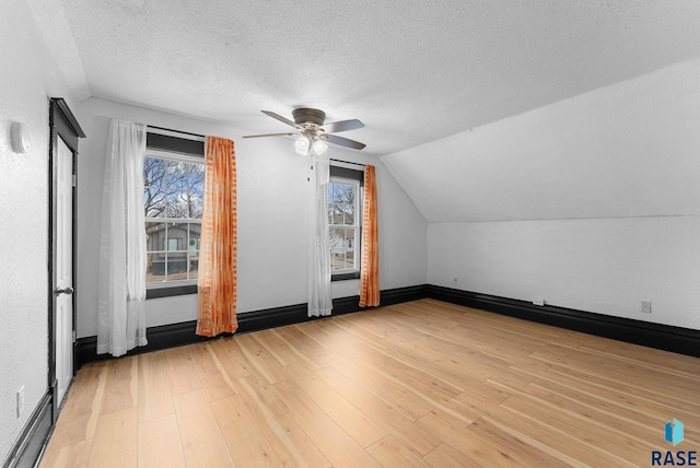 additional living space featuring light wood-type flooring, a textured ceiling, and vaulted ceiling