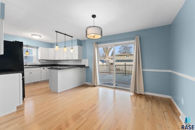 kitchen with black refrigerator, backsplash, light hardwood / wood-style flooring, white cabinets, and hanging light fixtures