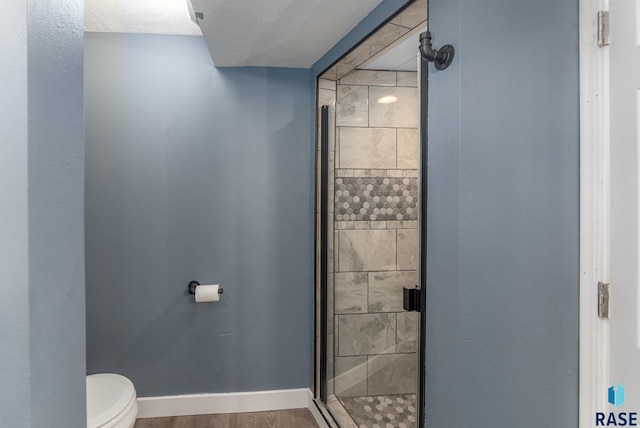 bathroom with wood-type flooring, a shower with shower door, and toilet