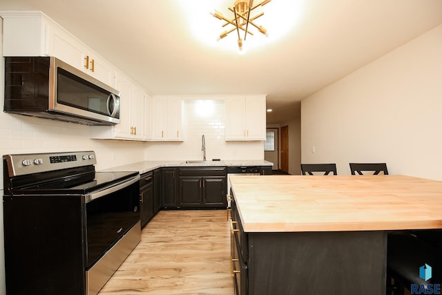 kitchen featuring white cabinetry, sink, stainless steel appliances, a notable chandelier, and light wood-type flooring