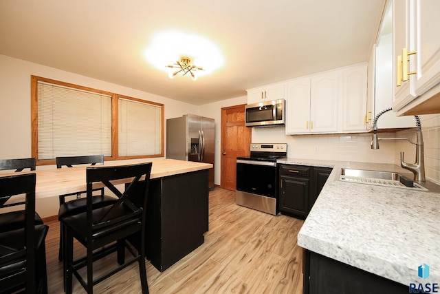 kitchen with white cabinets, sink, light hardwood / wood-style flooring, decorative backsplash, and appliances with stainless steel finishes