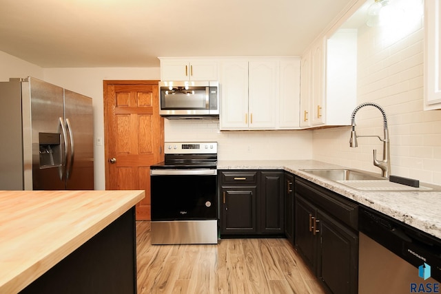 kitchen with white cabinets, sink, light hardwood / wood-style flooring, appliances with stainless steel finishes, and light stone counters