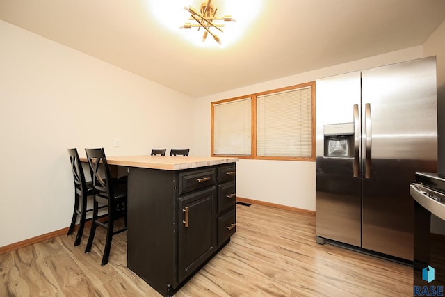 kitchen featuring an inviting chandelier, light wood-type flooring, appliances with stainless steel finishes, a kitchen island, and a breakfast bar area