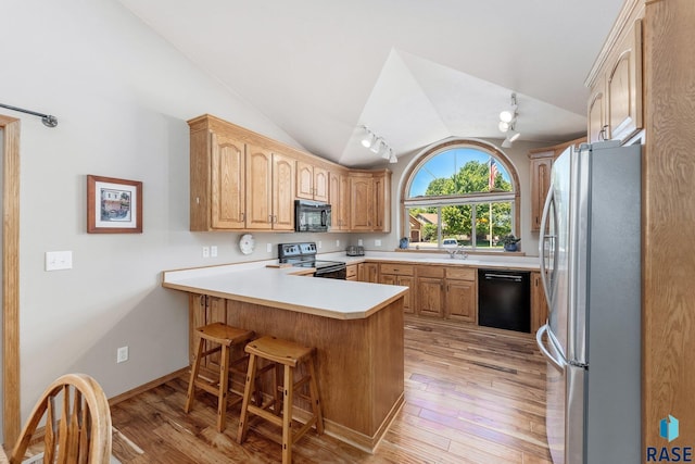 kitchen with kitchen peninsula, vaulted ceiling, a breakfast bar, black appliances, and light wood-type flooring