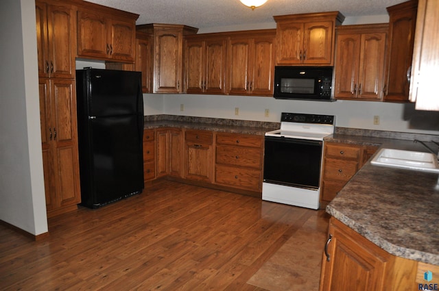 kitchen featuring dark wood-type flooring, sink, black appliances, and a textured ceiling