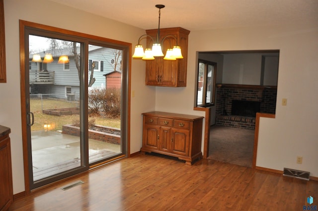 interior space with a brick fireplace, a chandelier, and light wood-type flooring