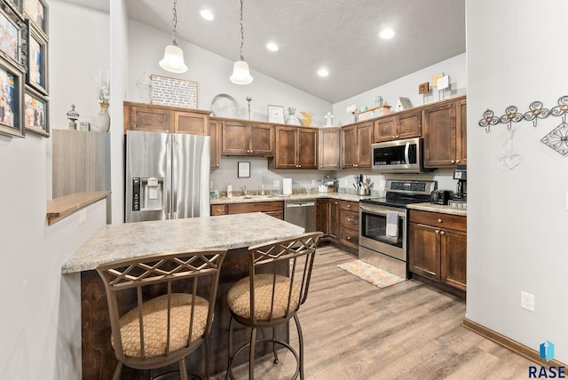 kitchen featuring a kitchen breakfast bar, light hardwood / wood-style floors, pendant lighting, vaulted ceiling, and appliances with stainless steel finishes