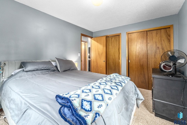 bedroom with a textured ceiling, light colored carpet, and two closets