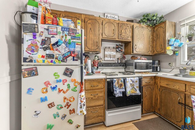 kitchen with a textured ceiling, white appliances, light hardwood / wood-style floors, and sink