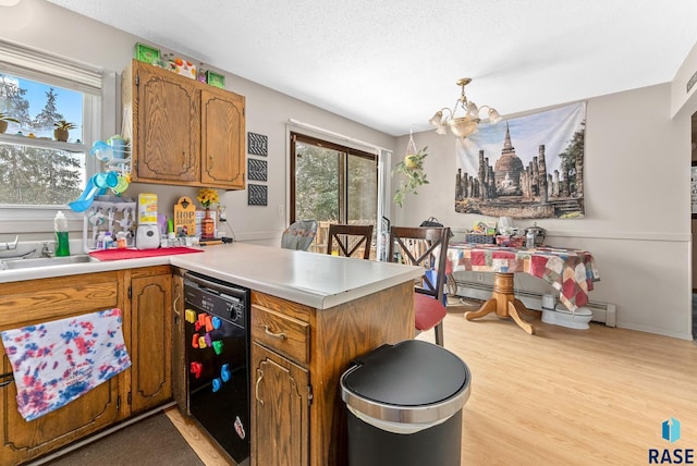 kitchen featuring black dishwasher, a notable chandelier, kitchen peninsula, light hardwood / wood-style floors, and decorative light fixtures