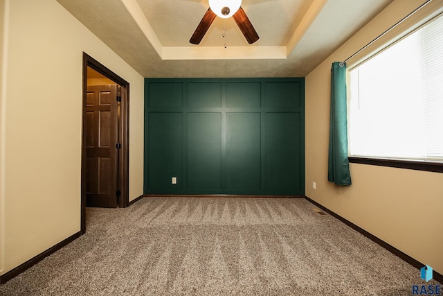 unfurnished bedroom with a tray ceiling, ceiling fan, and light carpet