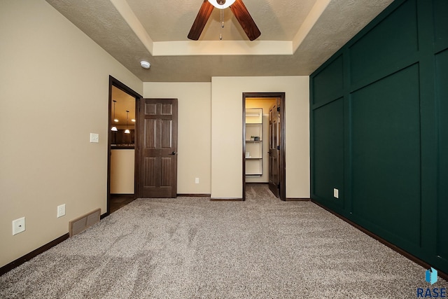 unfurnished bedroom with a spacious closet, ceiling fan, a raised ceiling, carpet floors, and a closet