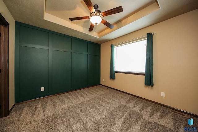 carpeted spare room featuring a tray ceiling and ceiling fan