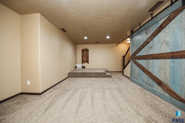 basement featuring a textured ceiling, a barn door, and carpet floors