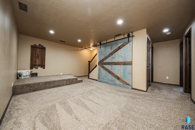 interior space with a textured ceiling, a barn door, and light colored carpet