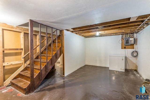 basement featuring a textured ceiling, electric panel, and fridge