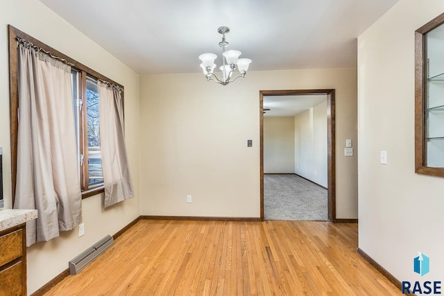 unfurnished room with light wood-type flooring, an inviting chandelier, and baseboard heating