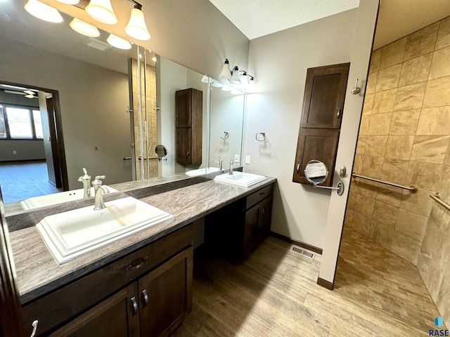 bathroom featuring a tile shower, hardwood / wood-style flooring, ceiling fan, and vanity