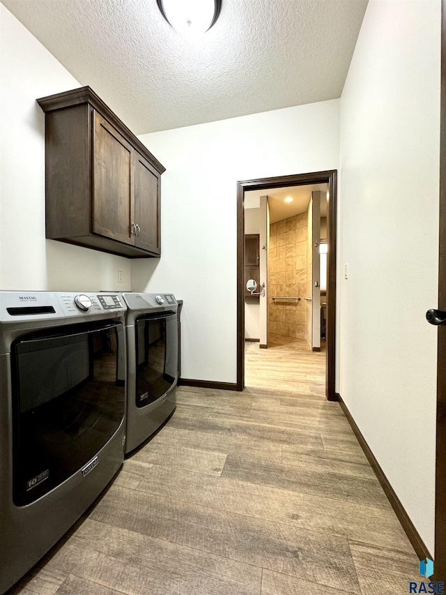 laundry room featuring a textured ceiling, light hardwood / wood-style flooring, cabinets, and independent washer and dryer