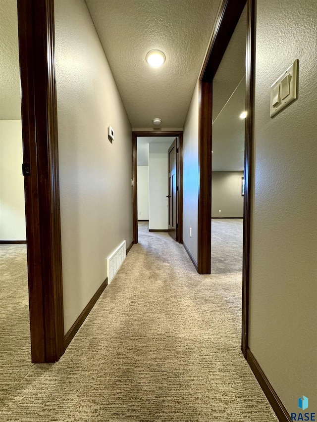 hall with light colored carpet and a textured ceiling