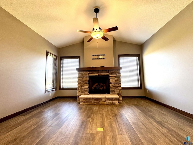 unfurnished living room with ceiling fan, wood-type flooring, vaulted ceiling, and a stone fireplace