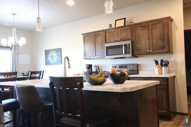 kitchen featuring pendant lighting, hardwood / wood-style floors, appliances with stainless steel finishes, a notable chandelier, and a kitchen bar