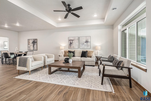 living room featuring hardwood / wood-style floors, a tray ceiling, and ceiling fan