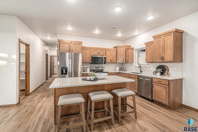 kitchen with appliances with stainless steel finishes, a breakfast bar, sink, light hardwood / wood-style flooring, and a kitchen island