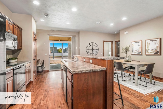 kitchen featuring sink, hardwood / wood-style floors, a textured ceiling, a kitchen island with sink, and appliances with stainless steel finishes