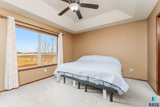 carpeted bedroom featuring a tray ceiling and ceiling fan