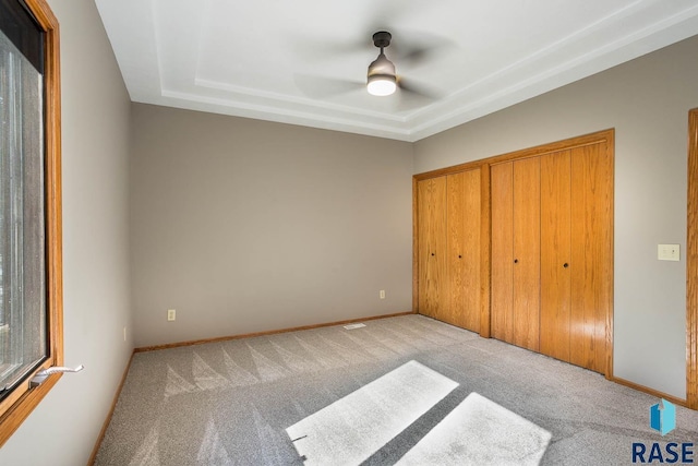 unfurnished bedroom featuring a raised ceiling, ceiling fan, a closet, and light carpet