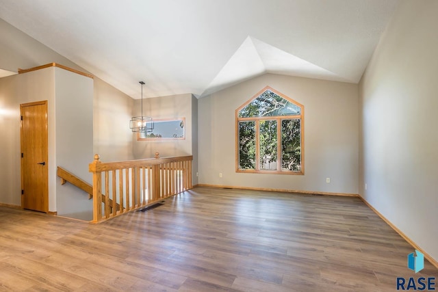 unfurnished room featuring hardwood / wood-style floors, lofted ceiling, and a chandelier