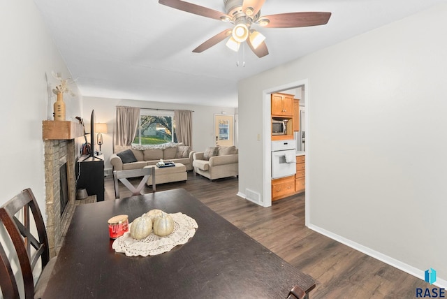 dining room with a fireplace, ceiling fan, and dark wood-type flooring