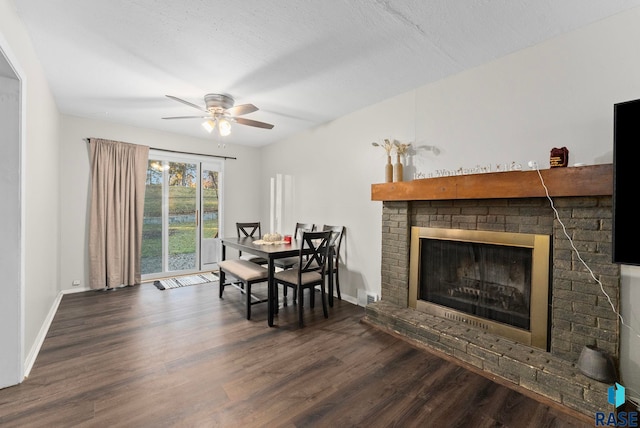 dining space featuring a textured ceiling, ceiling fan, a fireplace, and dark wood-type flooring