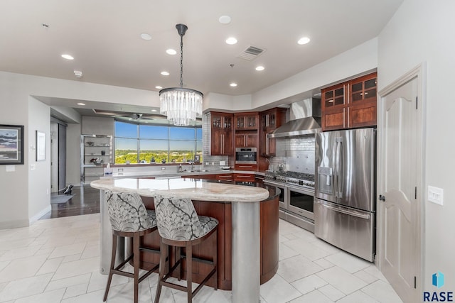 kitchen featuring light stone countertops, stainless steel appliances, wall chimney range hood, tasteful backsplash, and a kitchen island