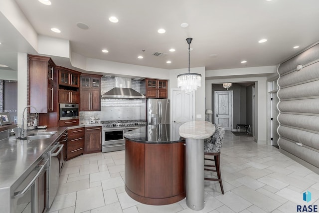 kitchen with sink, stainless steel appliances, wall chimney range hood, a chandelier, and a kitchen island