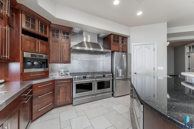 kitchen featuring dark stone counters, stainless steel appliances, tasteful backsplash, and wall chimney exhaust hood