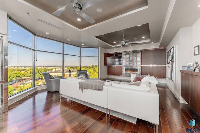 living room featuring a raised ceiling, floor to ceiling windows, plenty of natural light, and ceiling fan