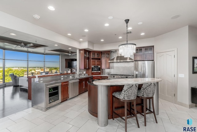 kitchen with wall chimney exhaust hood, stainless steel appliances, wine cooler, kitchen peninsula, and pendant lighting