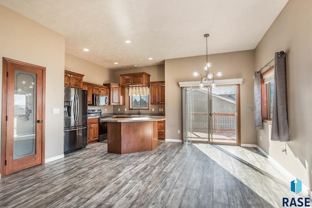 kitchen with stainless steel appliances, pendant lighting, a notable chandelier, light hardwood / wood-style floors, and a kitchen island