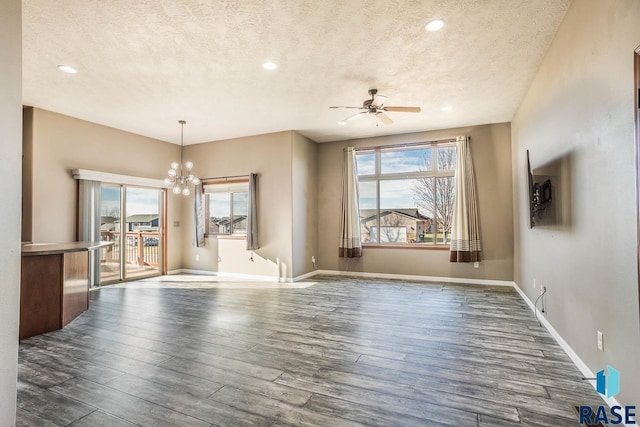 interior space featuring ceiling fan with notable chandelier, a healthy amount of sunlight, a textured ceiling, and dark wood-type flooring