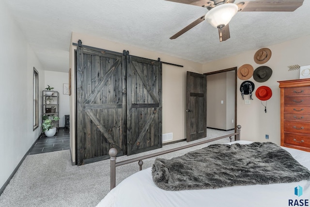 carpeted bedroom with a textured ceiling, a barn door, and ceiling fan