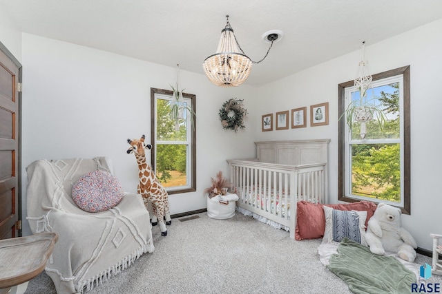 carpeted bedroom with a crib and a chandelier