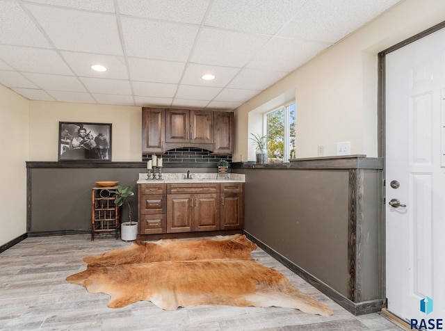 bar with backsplash, sink, a drop ceiling, and light hardwood / wood-style flooring