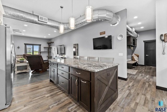 kitchen featuring pendant lighting, a center island, stainless steel fridge, light stone countertops, and dark brown cabinets