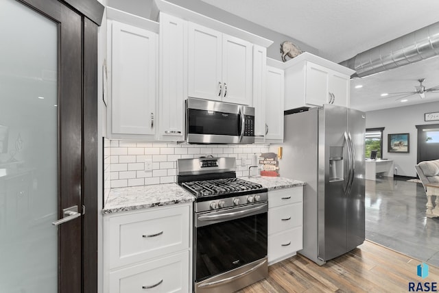 kitchen with appliances with stainless steel finishes, tasteful backsplash, ceiling fan, light hardwood / wood-style floors, and white cabinetry