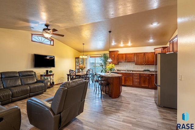 living room with ceiling fan with notable chandelier, light wood-type flooring, sink, and vaulted ceiling