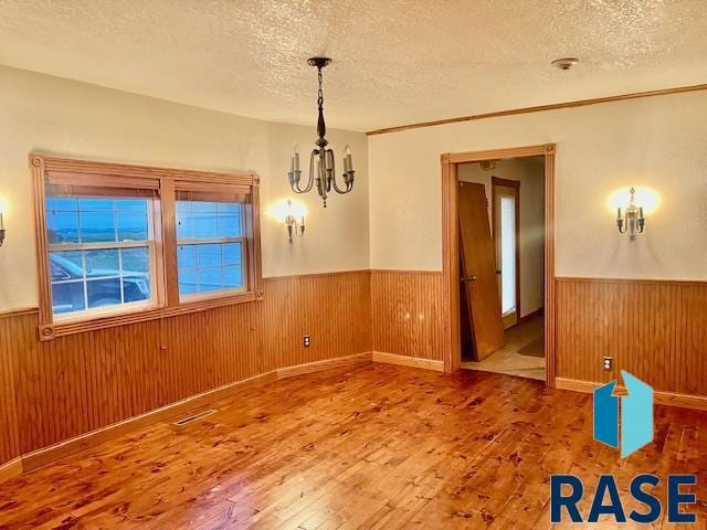 unfurnished room featuring wood-type flooring, a textured ceiling, and an inviting chandelier