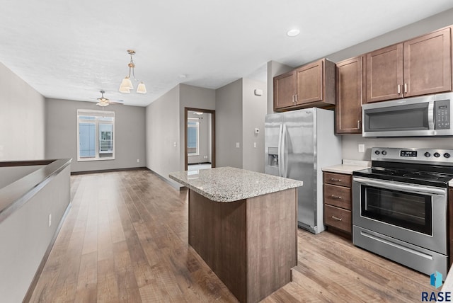 kitchen with appliances with stainless steel finishes, light wood-type flooring, ceiling fan, a kitchen island, and hanging light fixtures