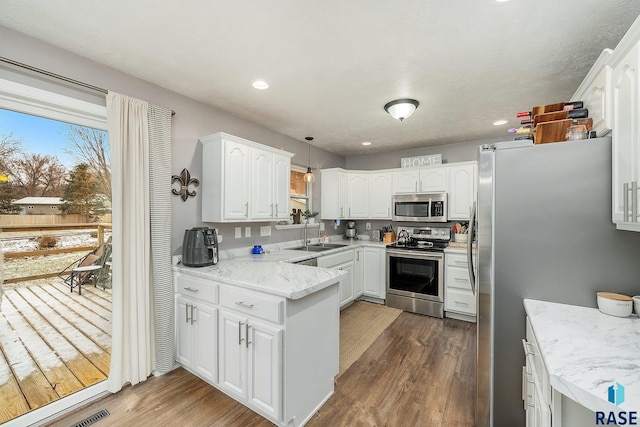 kitchen featuring appliances with stainless steel finishes, sink, dark hardwood / wood-style floors, white cabinetry, and hanging light fixtures